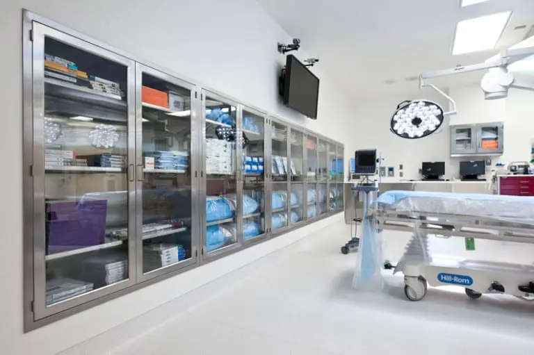 Modern STEM lab with white storage cabinets, a central table with microscopes, laptops and shelves full of samples.